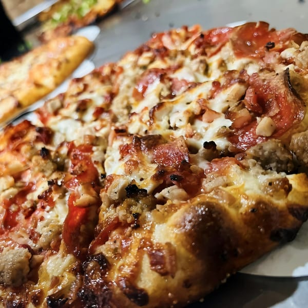 Close-up of a Task Force Pizza Co. pizza with pepperoni, chicken, and bacon.