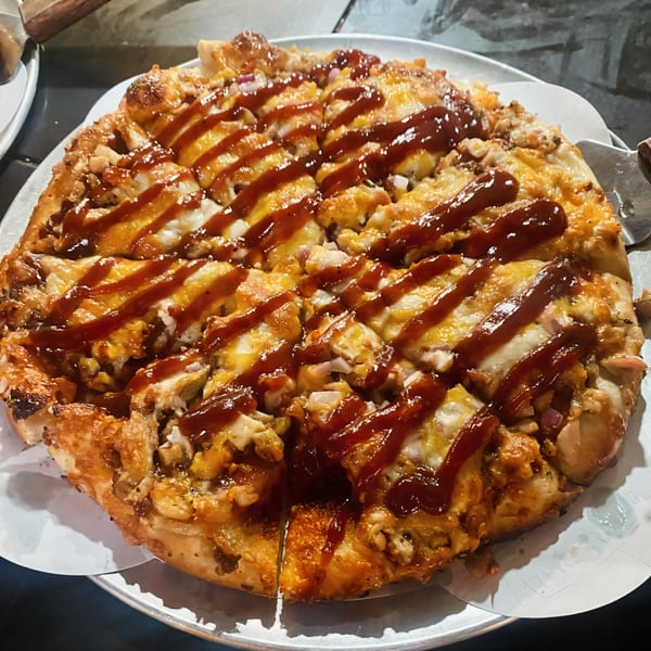 A whole BBQ chicken pizza with a drizzle of sauce, served on a metal pan.