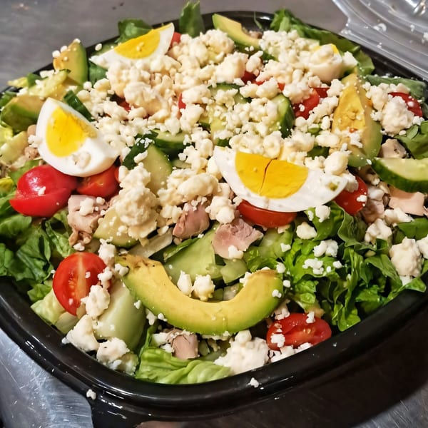 A vibrant Task Force Pizza Co. salad with lettuce, tomatoes, avocado, eggs, and feta cheese.