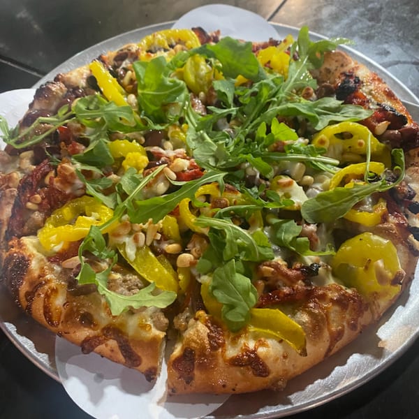 Task Force Pizza Co. pizza with arugula, yellow peppers, and pine nuts on a metal tray.