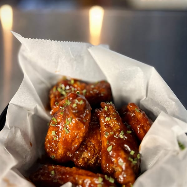Sweet and spicy chicken wings from Task Force Pizza Co., garnished with chives in a paper-lined basket.